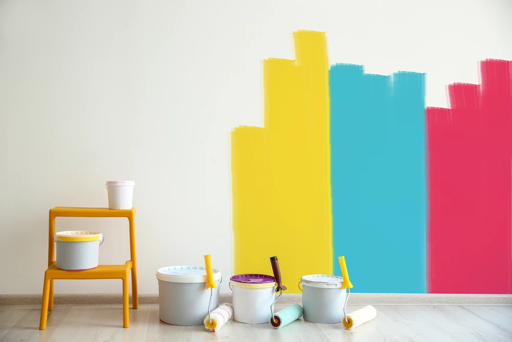 Intérieur résidentiel en cours de rénovation avec mur partiellement peint en bandes colorées jaune, turquoise et rose