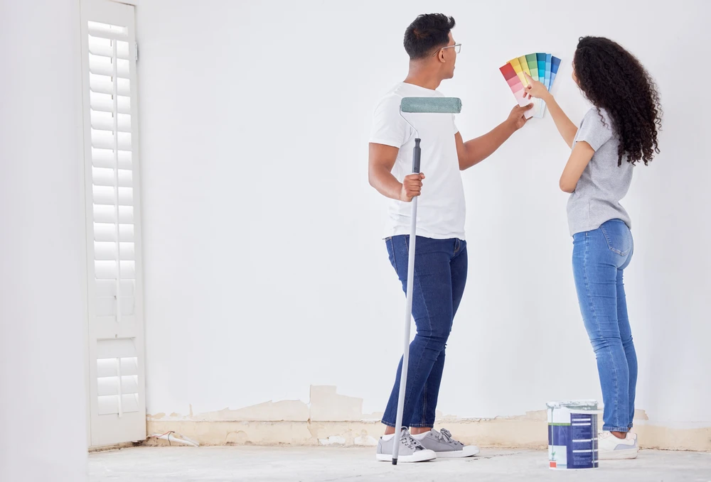Couple rénovant l'intérieur d'une maison, homme tenant rouleau à peinture, femme consultant nuancier couleurs